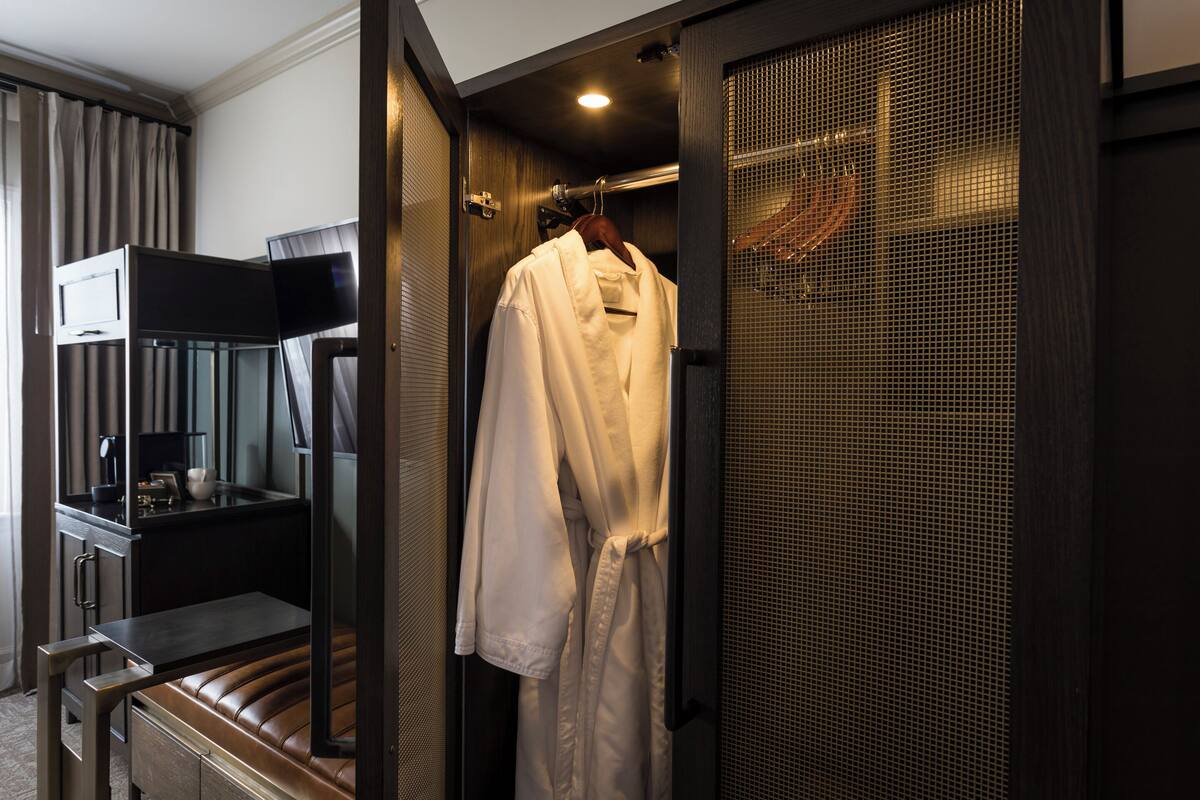Ein Hotelzimmer mit Sitzecke, Fernseher, aufgehängtem Bademantel und Duschbereich.