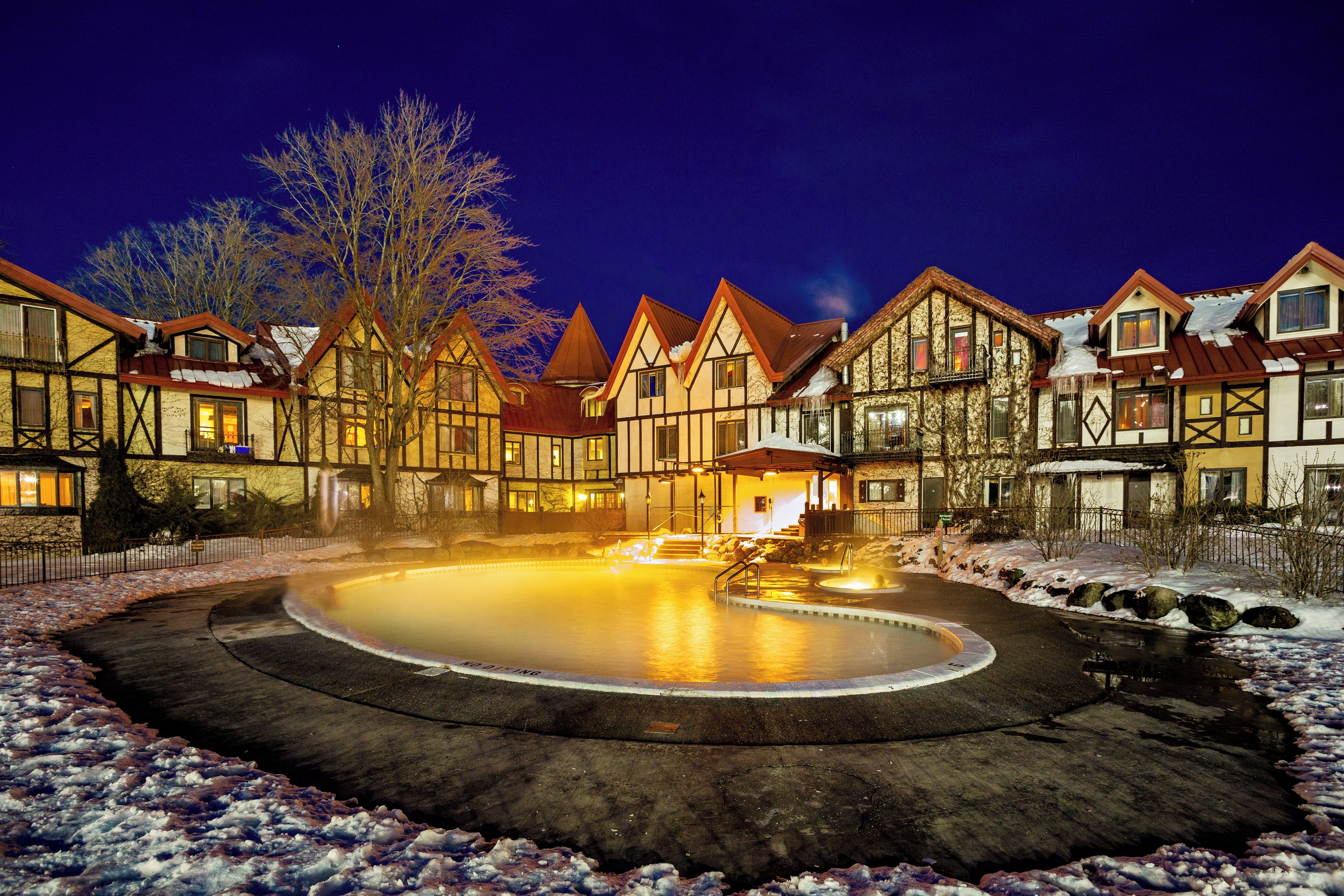 A traditional European-style hotel with multiple buildings, a central courtyard with a heated pool, and snow on the ground.