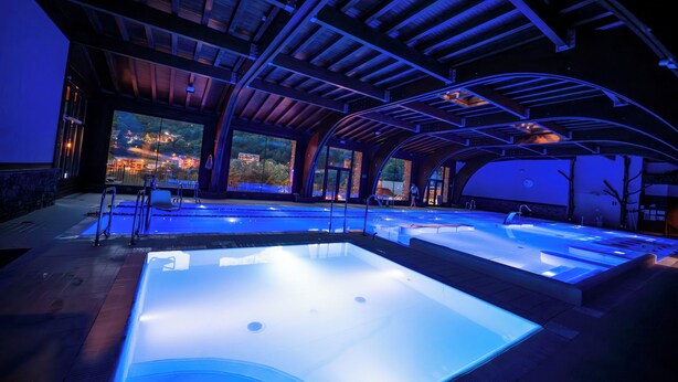 A large indoor swimming pool with clear water, surrounded by a modern architectural design with arched ceilings and large windows. - Anyospark Hotel (Anyos)