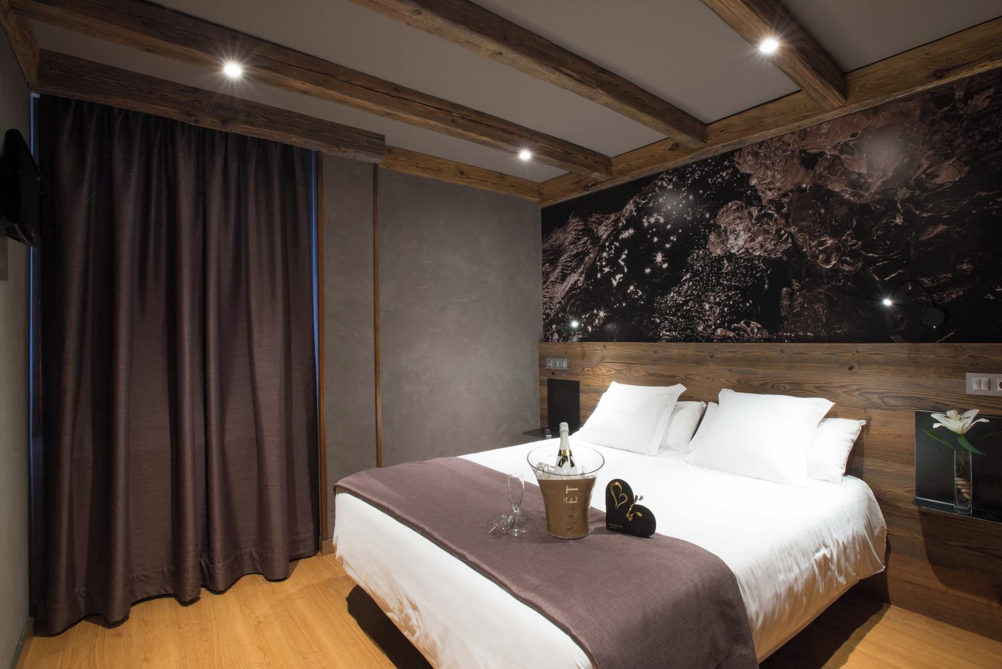 A bedroom with a bed, a nightstand, a bottle of champagne, and a wall with a celestial design.