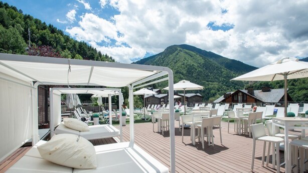 Terraza con sillones blancos y sombrillas, con vista a un paisaje montañoso.