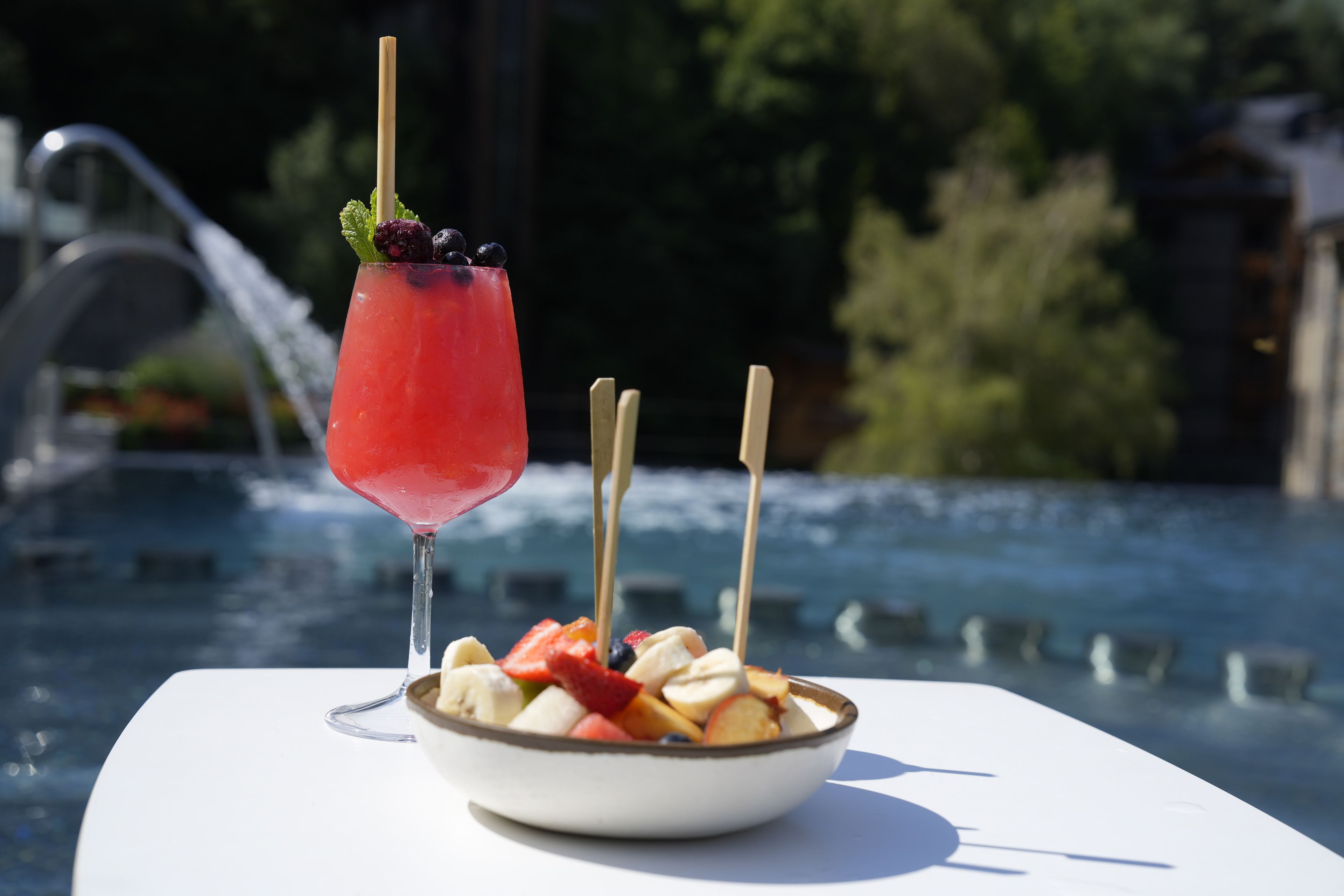 Een tafeltje bij het zwembad met een schaal fruit en een cocktailglas met rietje.