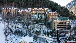 Una cabaña de varios pisos con fachada de piedra y múltiples balcones, rodeada por terreno nevado y montañas boscosas.
