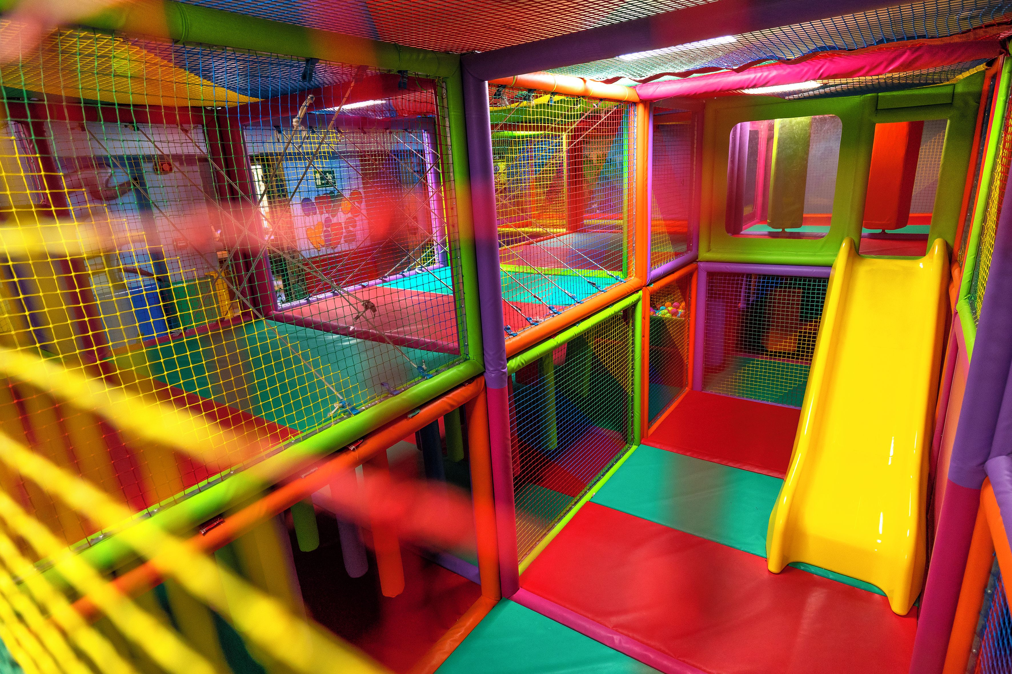 Un espace de jeux intérieur à plusieurs niveaux, doté de murs en filet et de toboggans.