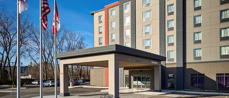A Hampton Inn hotel with a covered entrance, American flags, and a parking lot.