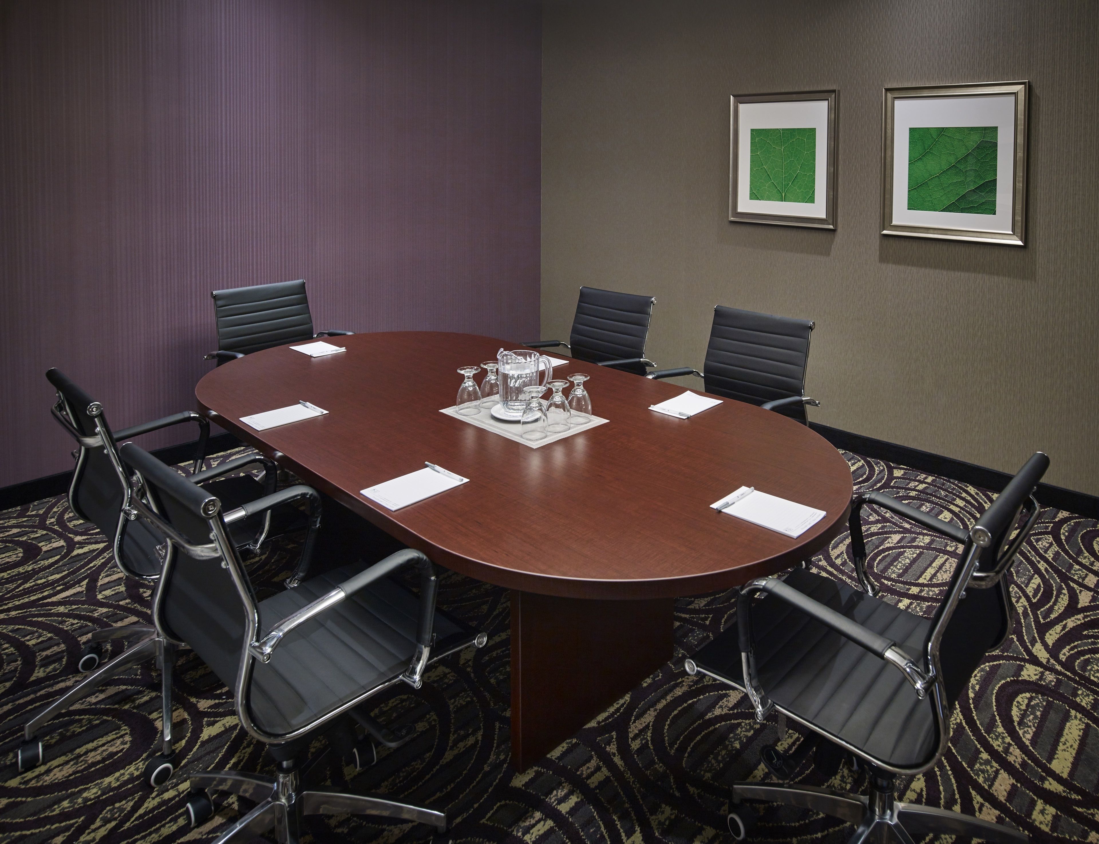 A conference room with a large oval table, six black chairs, and two framed botanical prints on the wall.