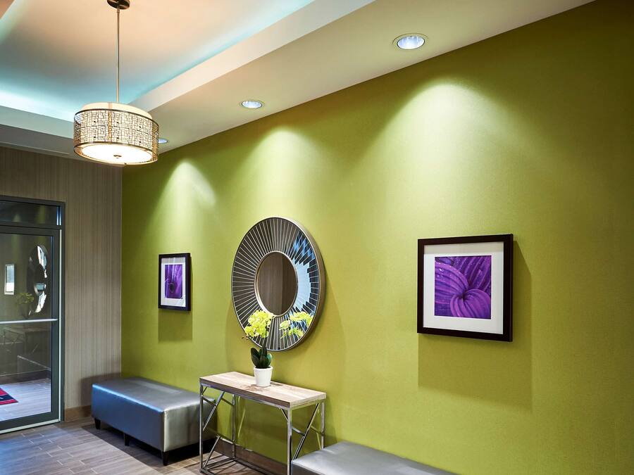 Un área de espera moderna con una pared verde, dos bancos, un espejo redondo y obras de arte enmarcadas.