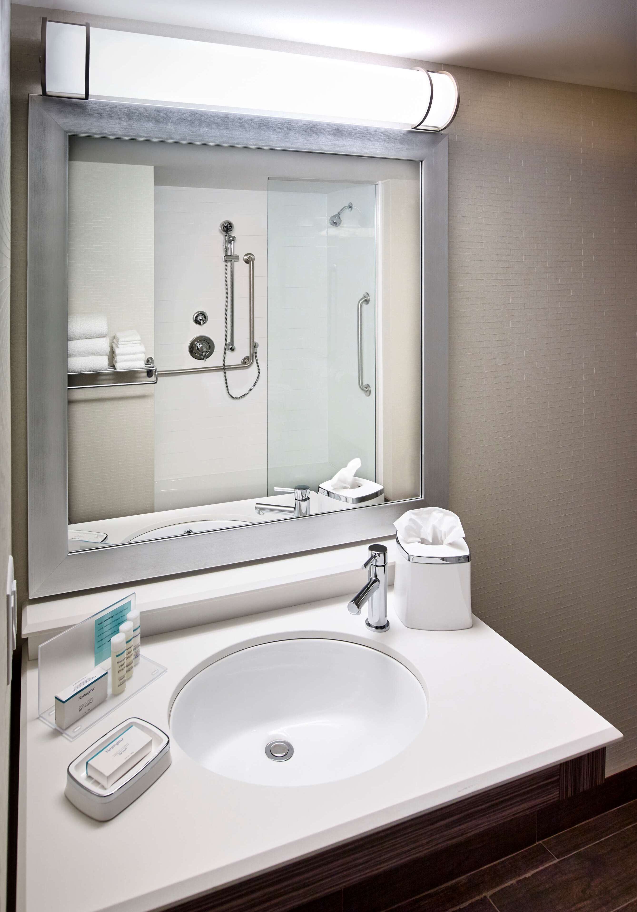 A modern bathroom with a large mirror, a white sink, a handheld showerhead, and a towel rack.