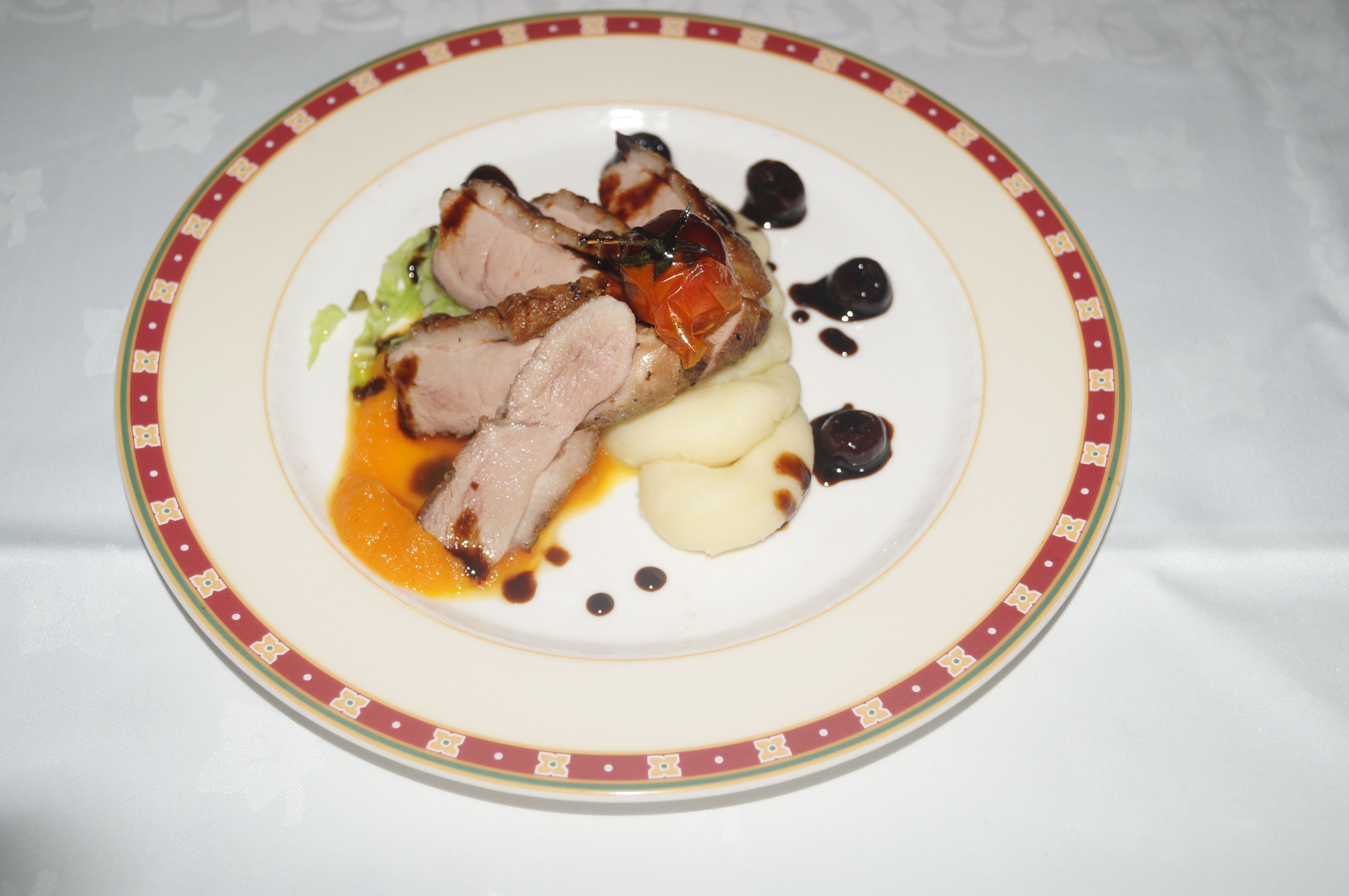 Un plato con carne en rodajas, puré de papas y verduras, decorado con salsa.