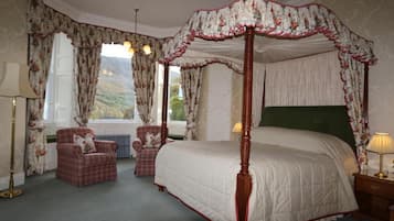 A four-poster canopy bed with a green headboard, two upholstered chairs, a floor lamp, and a view of the outdoors through large windows.