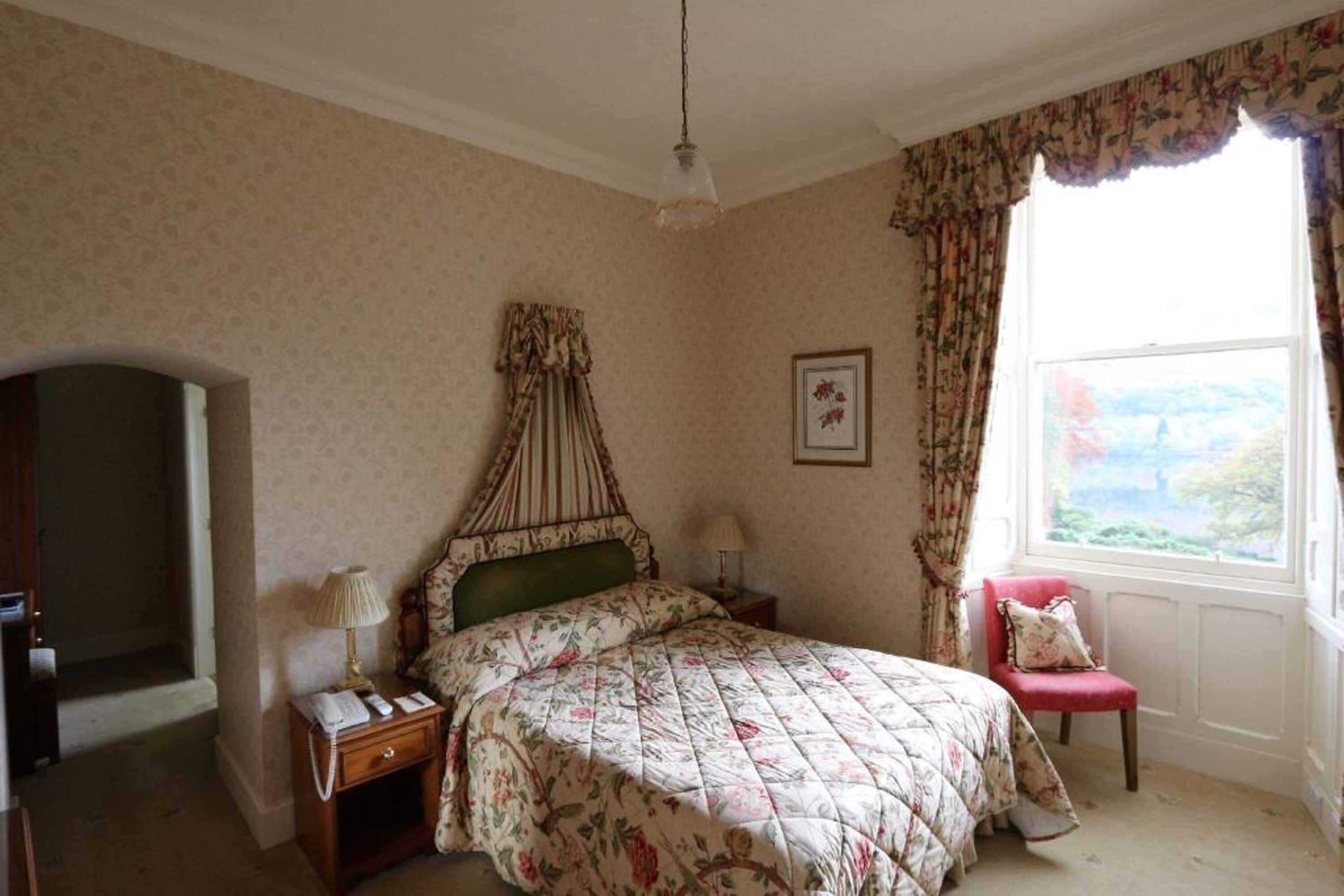 A bedroom with a bed, a nightstand, a chair, a window with curtains, and a framed picture on the wall.