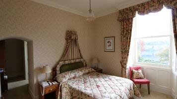 A bedroom with a bed, a nightstand, a chair, a window with curtains, and a framed picture on the wall.