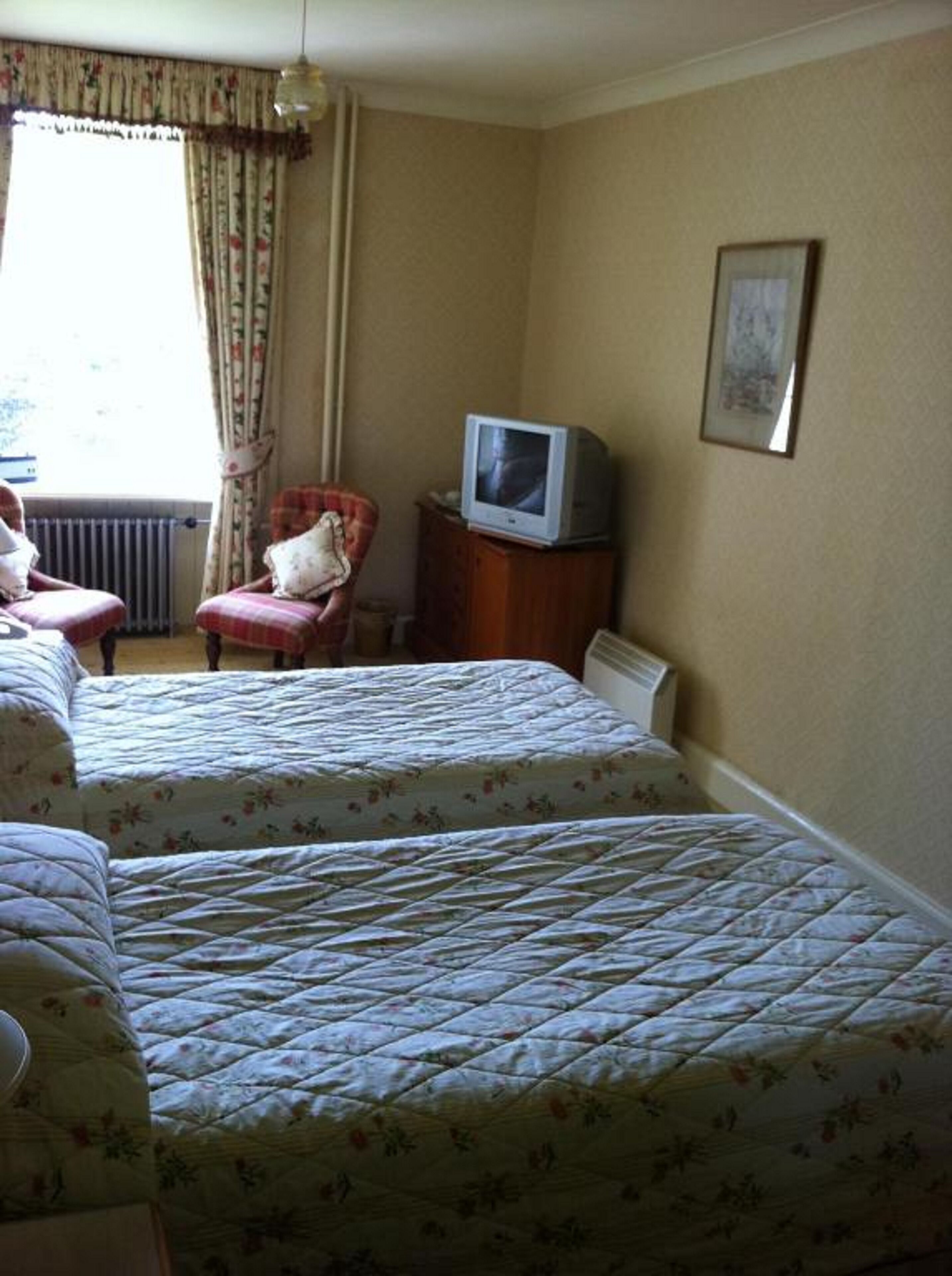 A hotel room with two beds, a chair, a television, and a radiator.