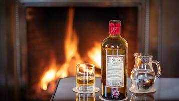 A bottle of Ben Nevis whisky, a glass of whisky, and a jug of water on a table in front of a fireplace.