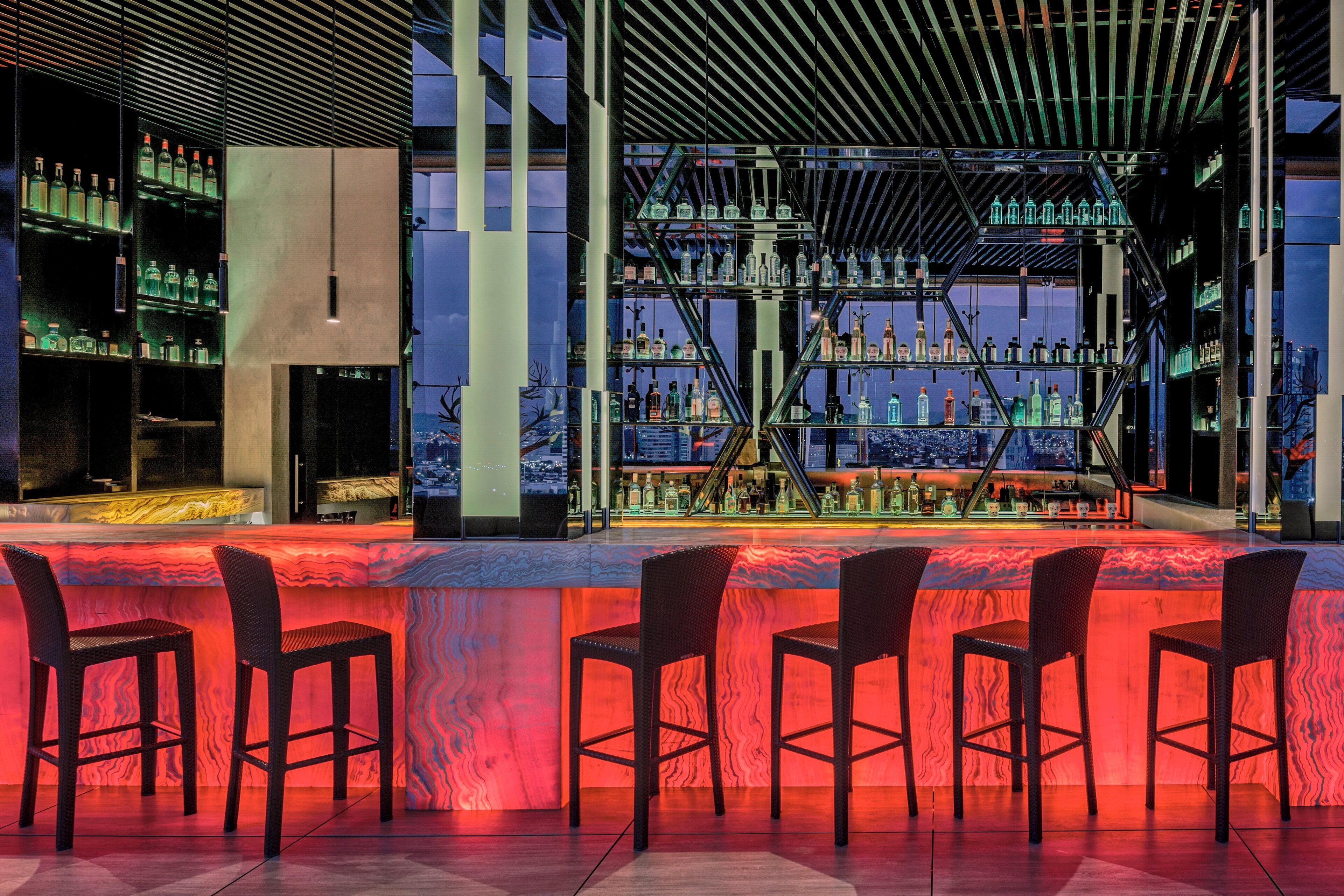 Una zona de bar con varias estanterías llenas de botellas, una barra y taburetes.