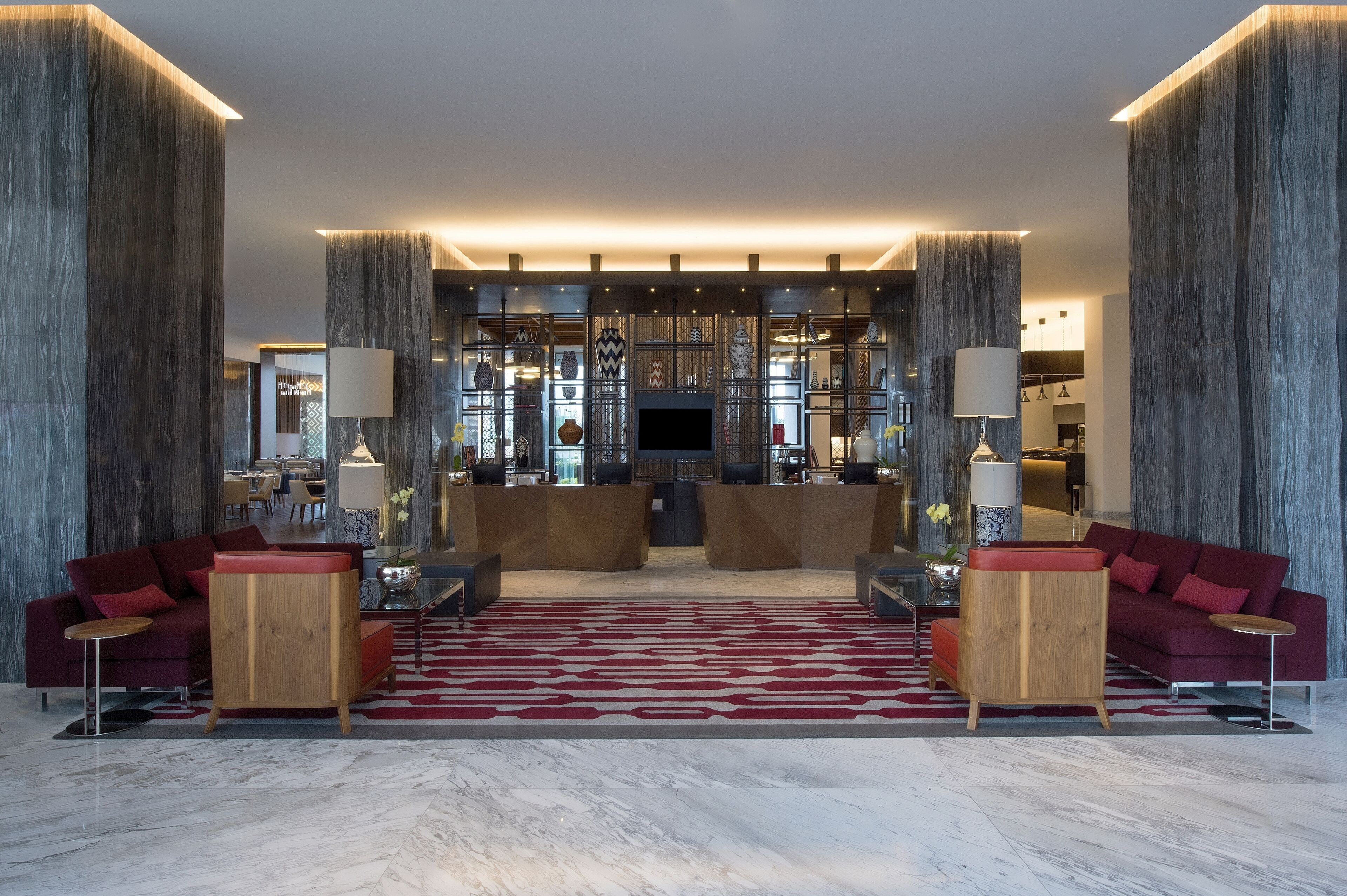 A spacious lobby with a central reception desk, red sofas, and a patterned carpet.