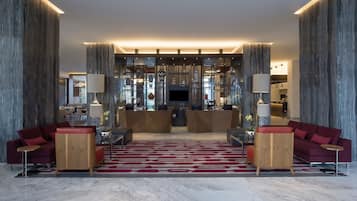 Un vestíbulo amplio con una recepción central, sofás rojos y una alfombra estampada.