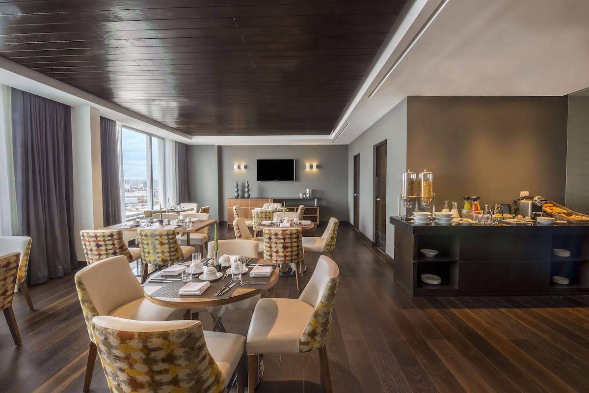 A modern dining area with round tables, cushioned chairs, a buffet station, and a city view.