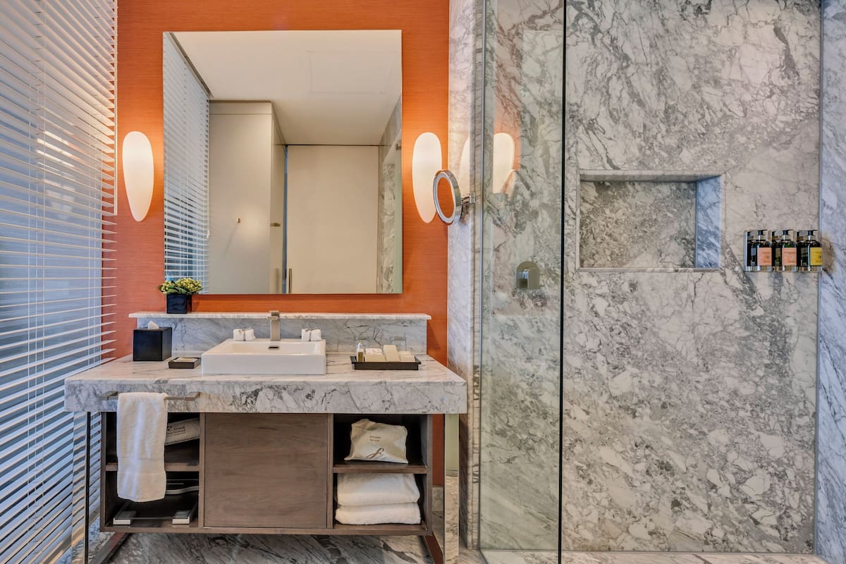 A modern bathroom with a marble sink, a large mirror, and a glass shower enclosure.