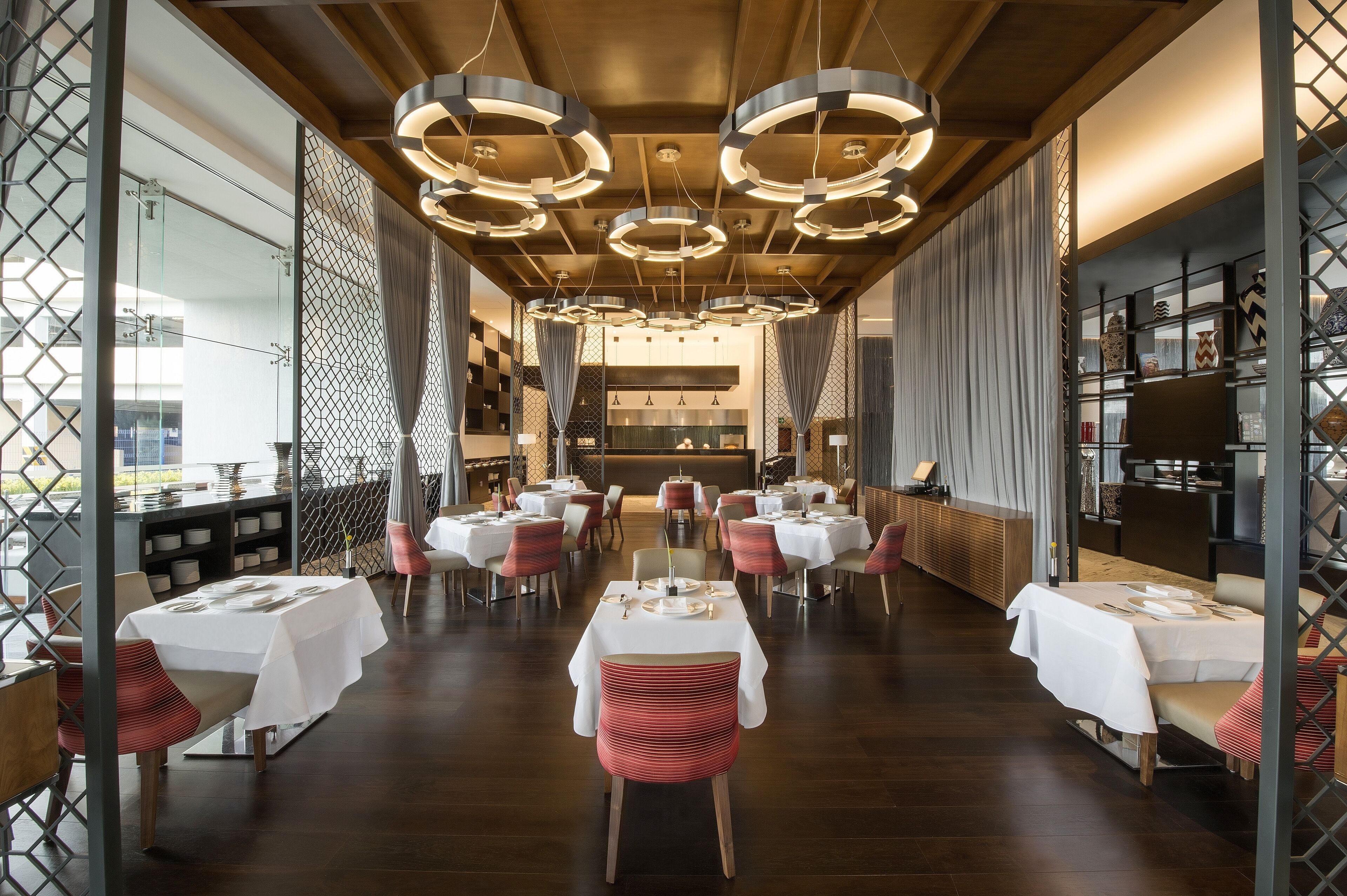 Un restaurante con luces redondas en el techo, manteles blancos y sillas rojas.