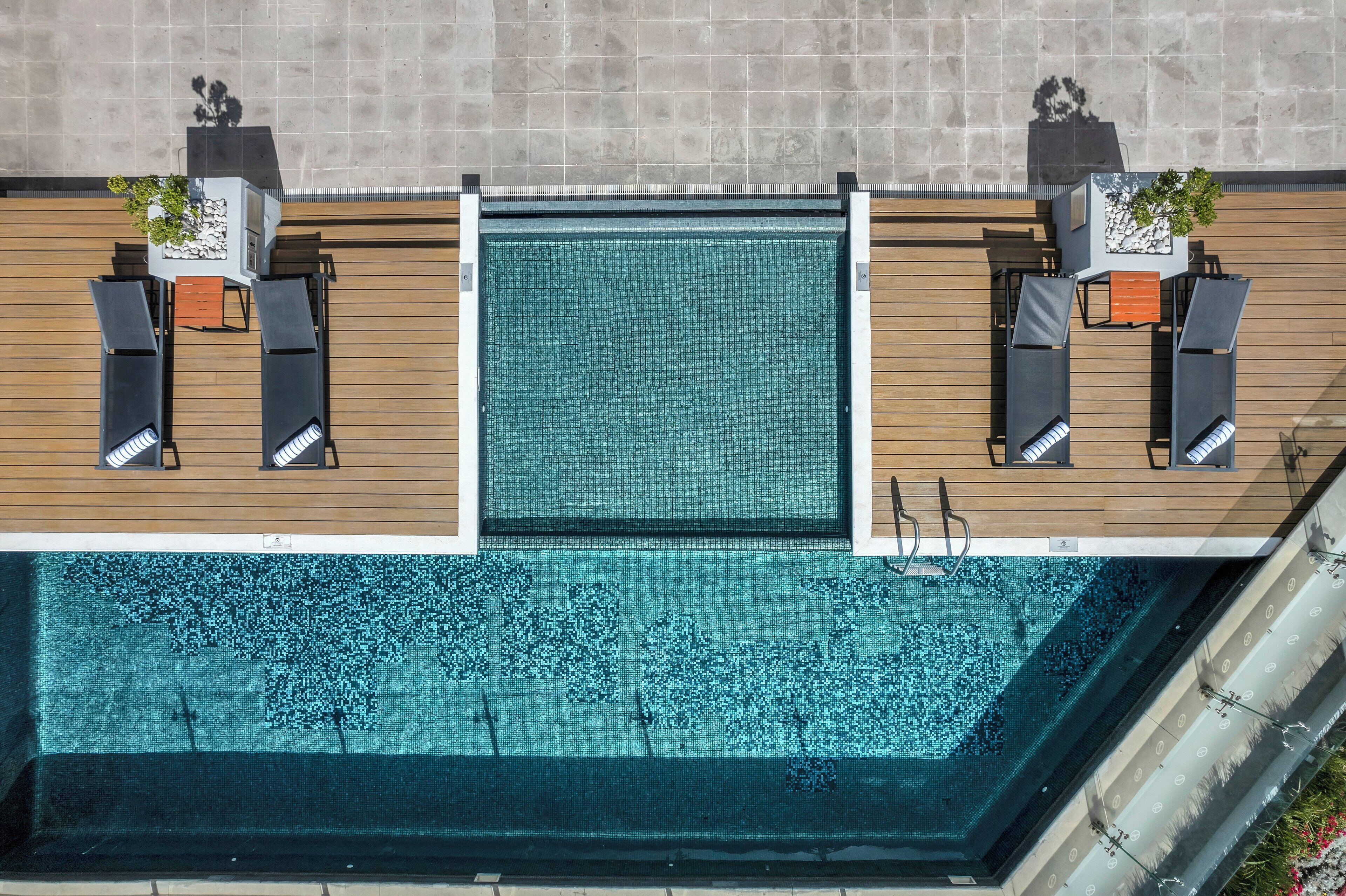 Vista aérea de una piscina en la azotea con dos zonas de estar, cada una con una silla y una planta en maceta.