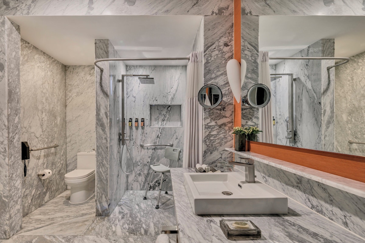 Un baño moderno con piso de mármol, un espejo grande, un lavamanos blanco y una zona de ducha.