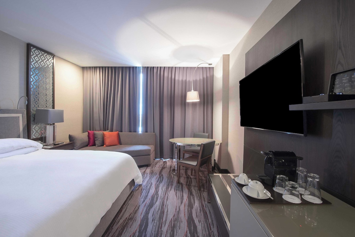 Una habitación de hotel con cama, sofá, mesa de comedor, televisión y cafetera.