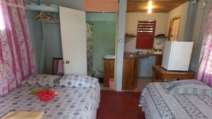 A bedroom with two beds, a small bathroom, and a kitchenette. - Beach Road Cottages at Jah Bs (Negril)