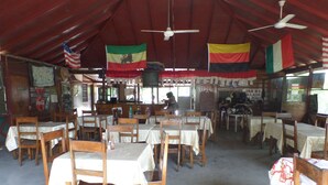 A restaurant with multiple tables and chairs, flags hanging from the ceiling, and a sign for 'JAH'S GALLERY'. - Beach Road Cottages at Jah Bs (Negril)