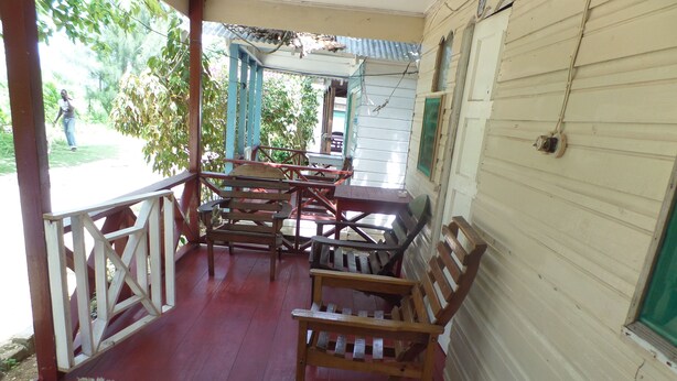 A covered porch with wooden furniture and a red floor. - Beach Road Cottages at Jah Bs (Negril)