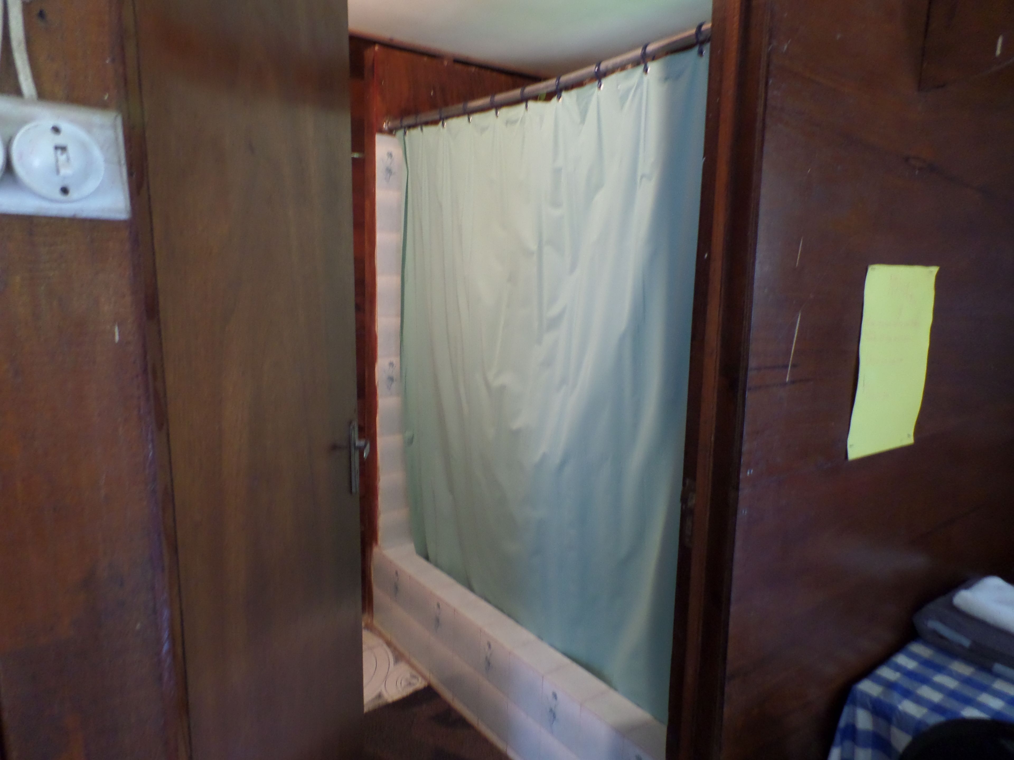 A bathroom with a shower curtain, a visible electrical outlet, and a piece of paper on the wall.