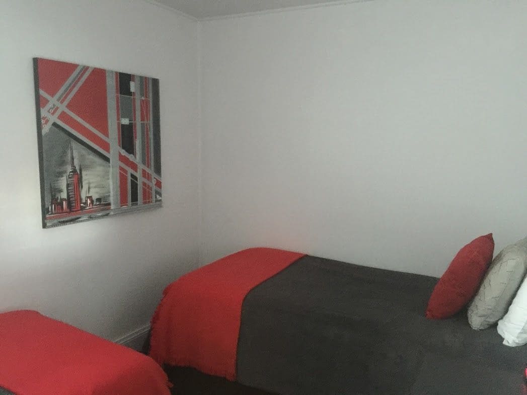 Ein Zimmer mit zwei Einzelbetten, jeweils mit einer roten und grauen Decke sowie einem roten Kissen. An der Wand hängt ein gerahmtes Bild.