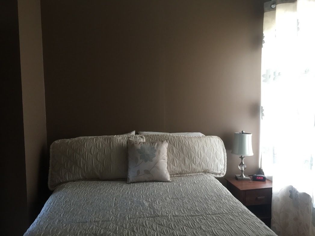 A bedroom with a large bed, a nightstand with a lamp, and a window with curtains.