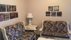 A room with two patterned sofas, a small table with a lamp, and wall art depicting wildlife. - Hôtel du Chasseur (Brownsburg-Chatham)
