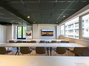 A conference room with a long table, chairs, a flat-screen TV, and a poster on the wall. - Ibis Styles Bordeaux Meriadeck (Bordeaux)