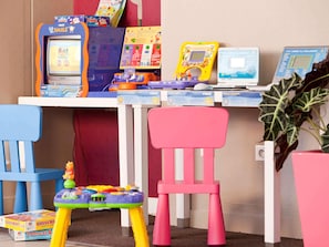 Zona infantil con juguetes educativos, una mesita y una silla rosa.