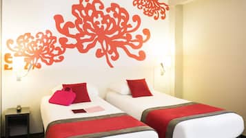A hotel room with two beds, each with a red pillow and a red blanket. There is a nightstand with a lamp and a phone on it. The walls have decorative red patterns.