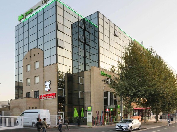 Un edificio moderno con fachada de vidrio, un restaurante llamado "La Boucherie Restaurant" en la planta baja y un letrero de "ibis Styles" en el nivel superior.
