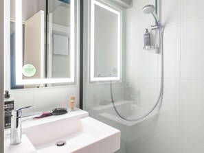 A bathroom with a white sink, a mirror with lights, a handheld showerhead, and toiletries. - Ibis Styles Bordeaux Meriadeck (Bordeaux)