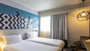 Habitación de hotel con dos camas, un escritorio, una silla, una lámpara y una ventana con cortinas.