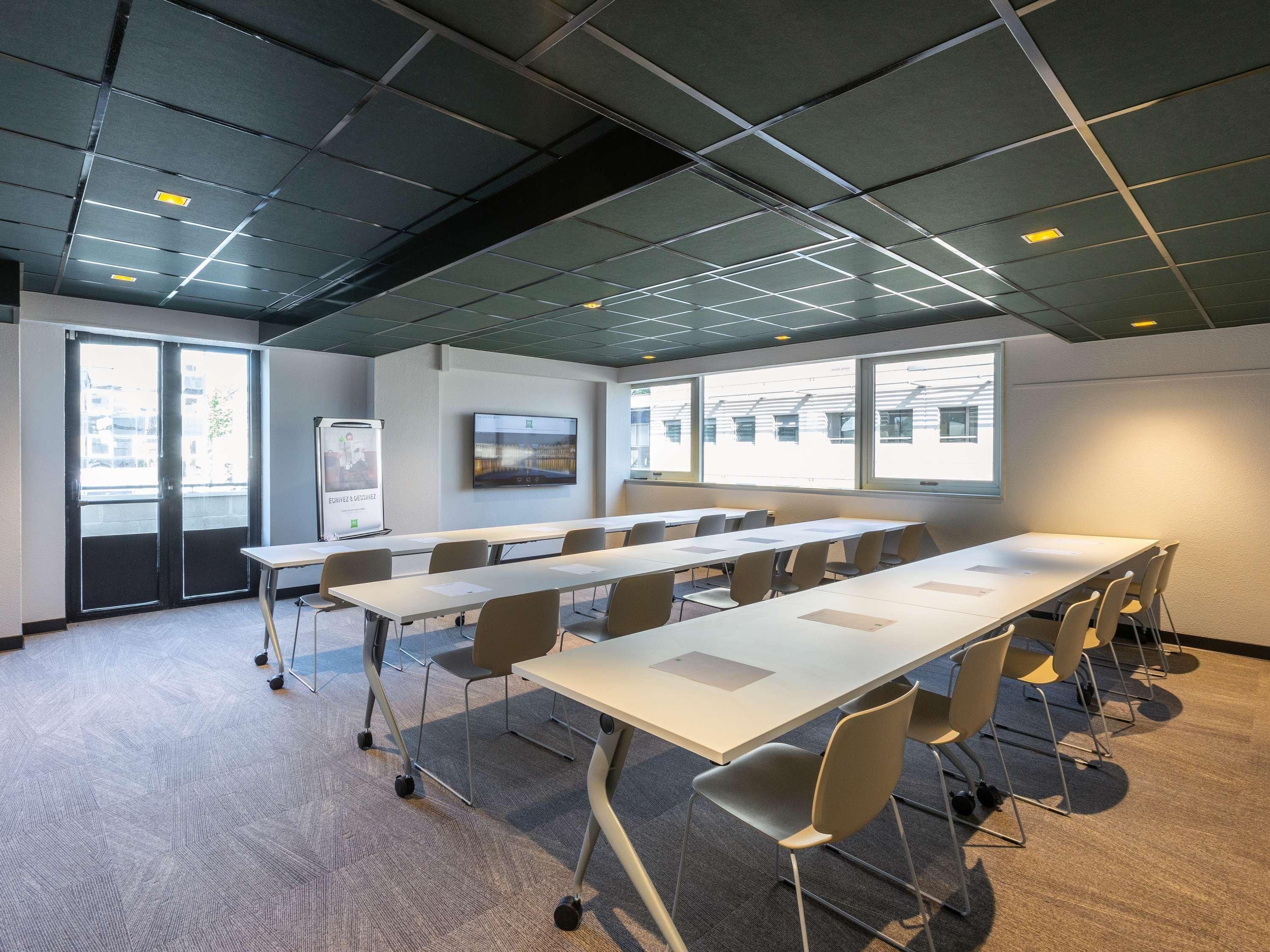 Un salón de conferencias con una amplia mesa, sillas, una pizarra y una pantalla para proyector.
