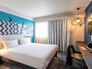 Habitación de hotel con una cama grande, un escritorio con una computadora portátil, una silla y una lámpara moderna.