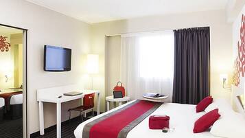 Habitación de hotel con cama, escritorio, silla, televisor y ventana con cortinas.