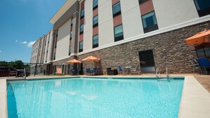 A hotel with a swimming pool, outdoor seating with umbrellas, and a stone facade.
