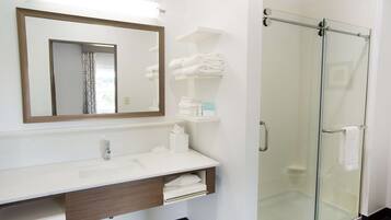 Une salle de bain moderne avec une douche à parois de verre, un lavabo blanc avec un miroir et des serviettes soigneusement pliées sur une étagère.