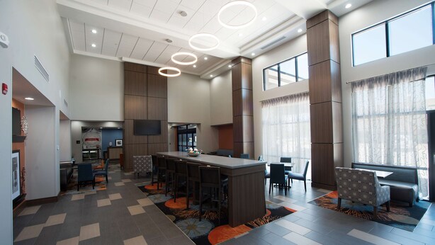 A modern hotel lobby with a central bar, seating areas, and large windows.