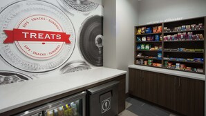 A kitchenette area with a wall-mounted refrigerator, a countertop, and a shelf stocked with snacks and sundries.