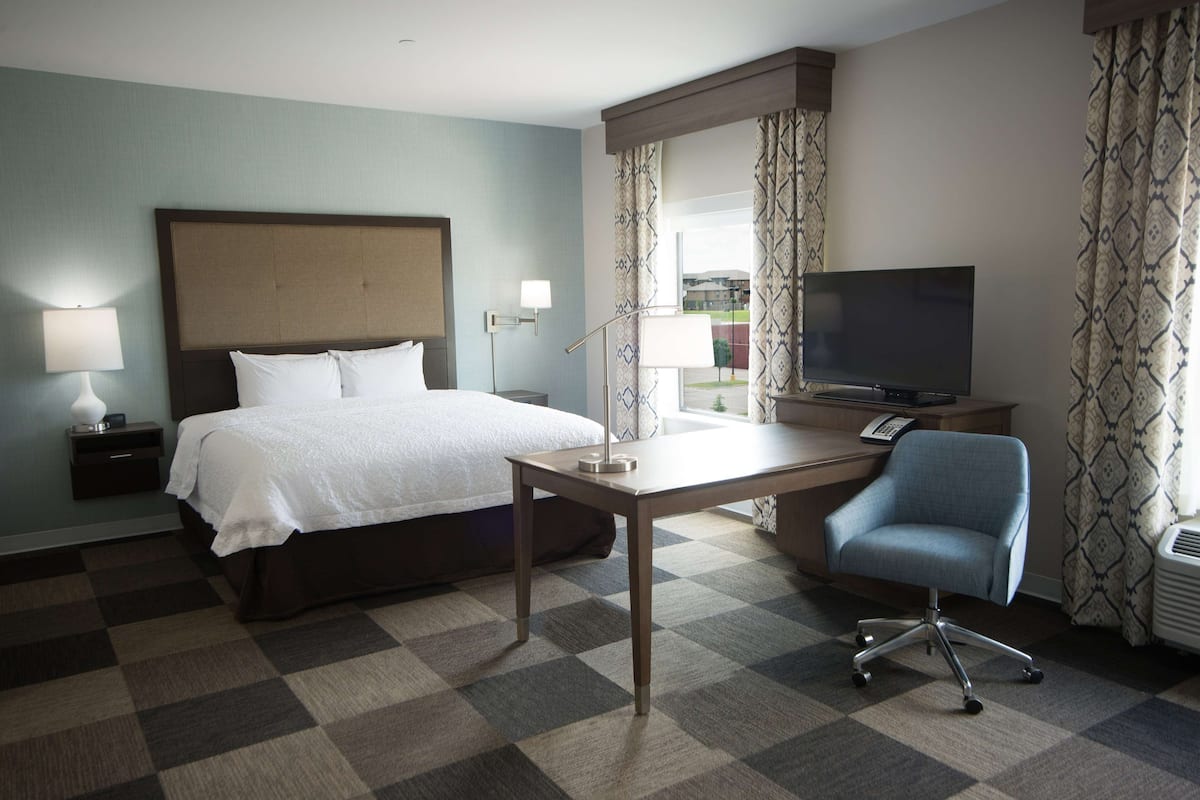 A hotel room with a bed, desk, chair, TV, and window with curtains.