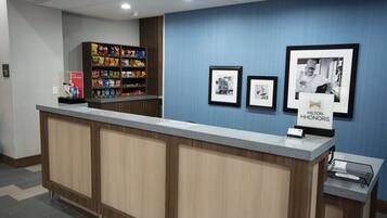 A hotel reception desk with a counter, a snack shelf, and framed pictures on the wall.