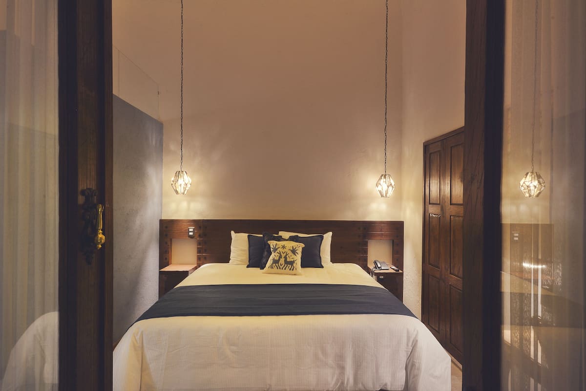 Una cama bien tendida con cabecera, dos lámparas de noche y una mesita de noche con un teléfono.